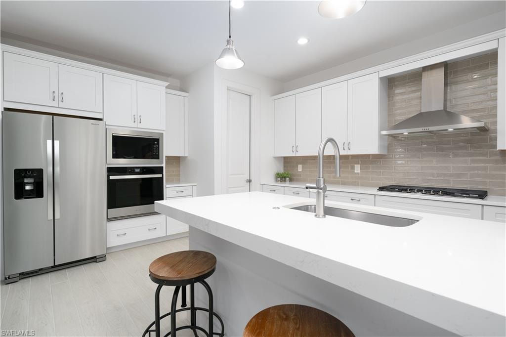 Kitchen with stainless steel appliances, hanging light fixtures, wall chimney range hood, white cabinetry, and recessed lighting