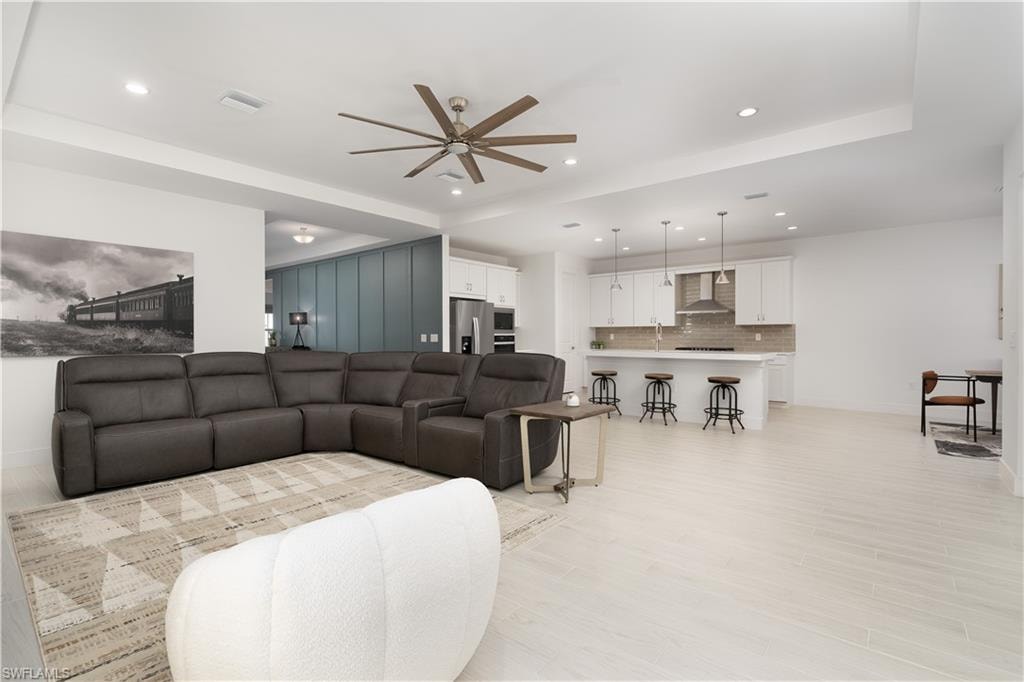 Living room with recessed lighting, light wood-style flooring, a raised ceiling, and a ceiling fan