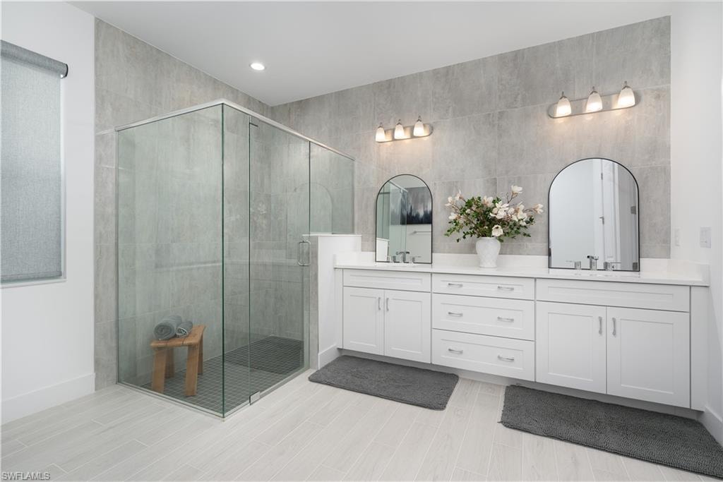 Full bathroom with double vanity, a shower stall, wood finish floors, and recessed lighting
