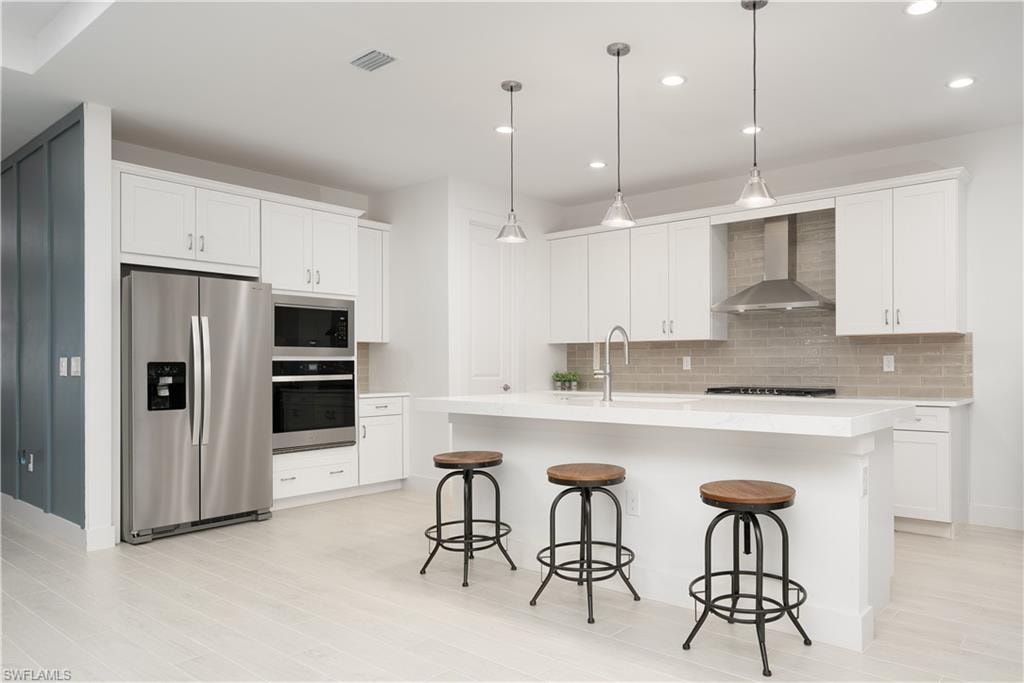Kitchen featuring stainless steel appliances, an island with sink, white cabinetry, and recessed lighting