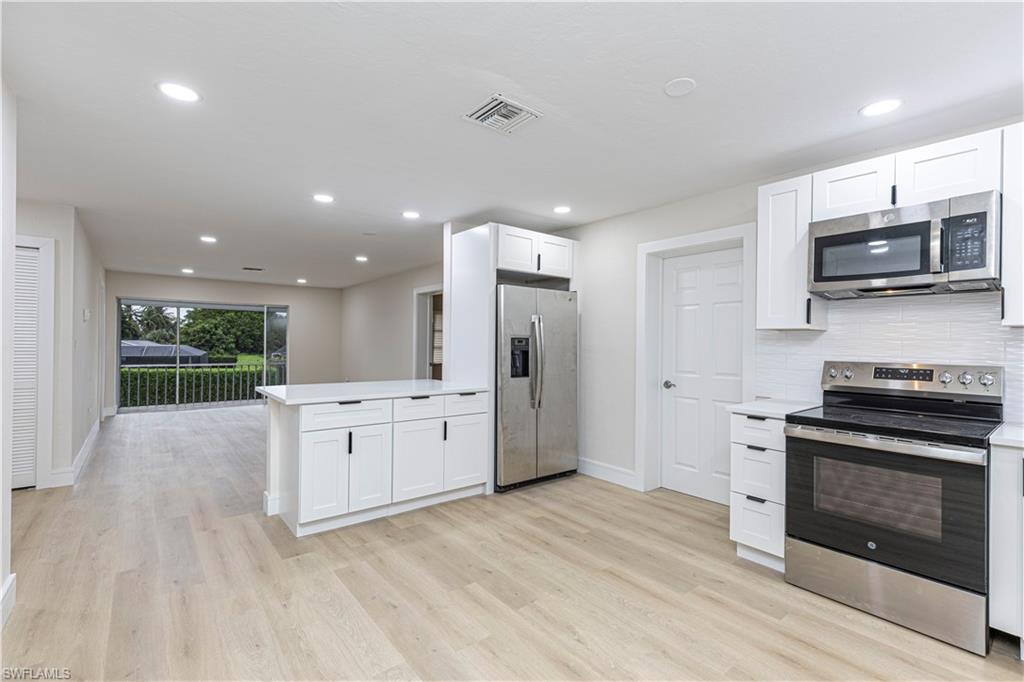 Kitchen featuring stainless steel appliances, a peninsula, white cabinetry, light wood-style flooring, and backsplash