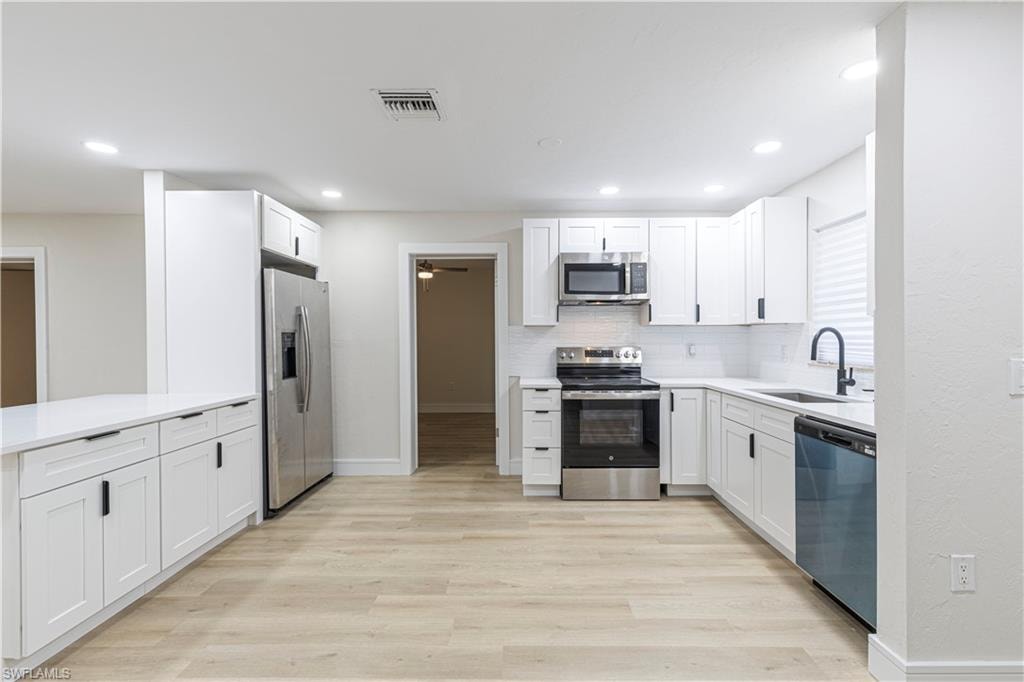 Kitchen with white cabinetry, stainless steel appliances, light wood-type flooring, decorative backsplash, and recessed lighting