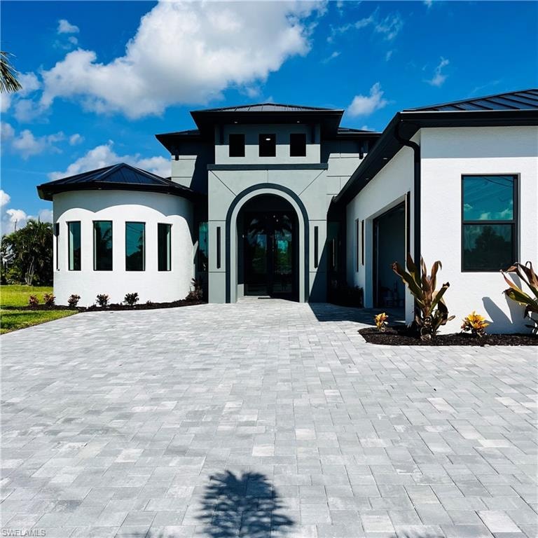 View of front facade featuring 10 ft clear galss double doors, stucco siding, a metal roof, and a standing seam roof