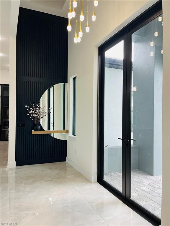 Hallway featuring french doors, a chandelier, and marble finish flooring