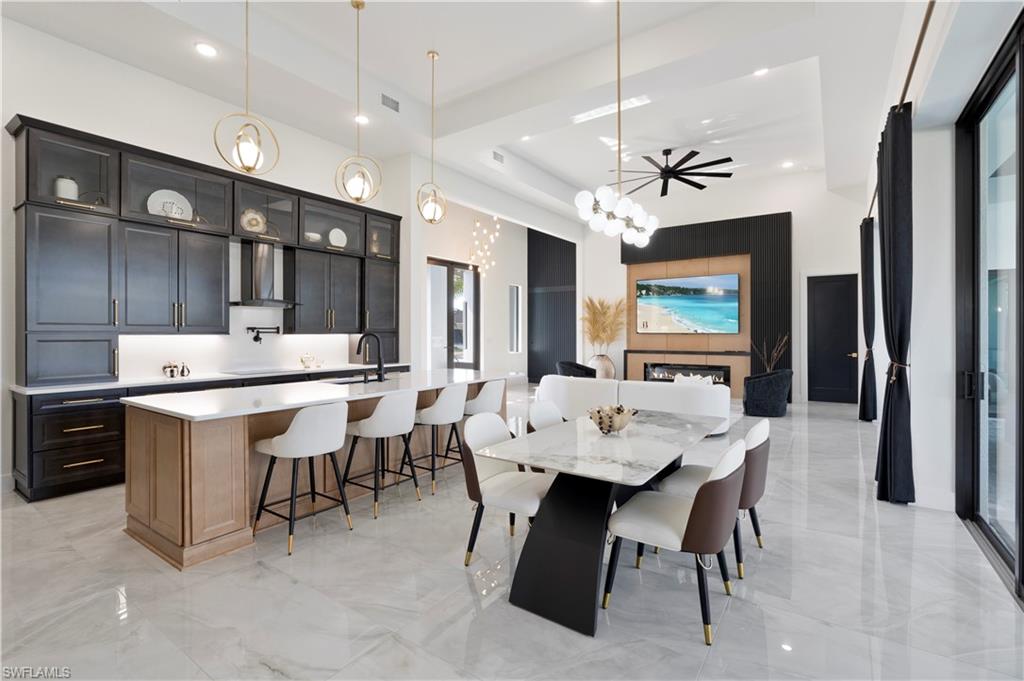 Dining room with a chandelier, a towering ceiling, a glass covered fireplace, light marble finish flooring, and a tray ceiling
