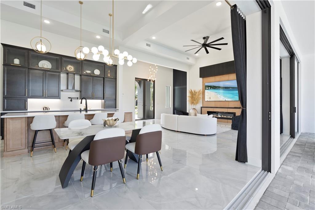 Dining area with a chandelier, ceiling fan, beamed ceiling, light marble finish floors, and a fireplace