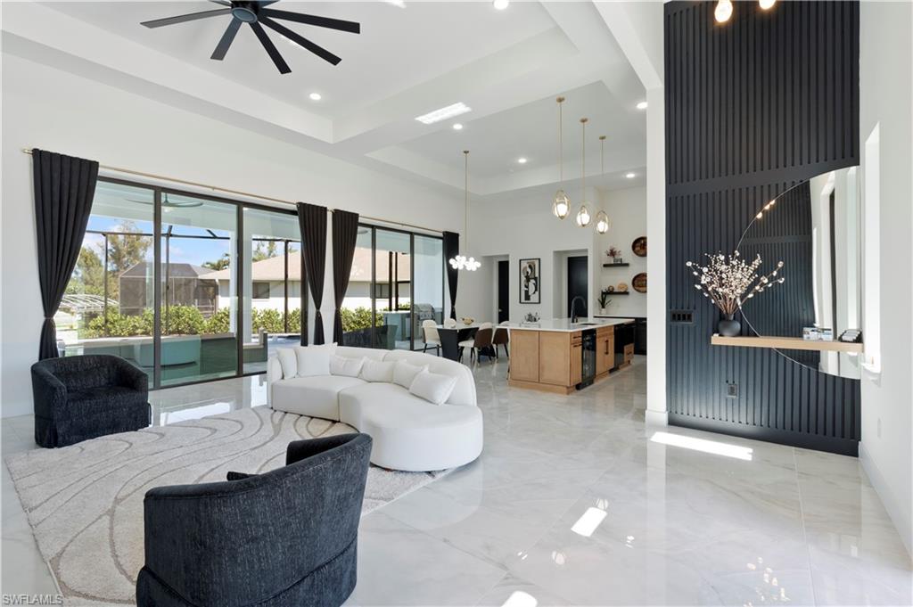 Living room featuring light marble finish flooring, a chandelier, a tray ceiling, recessed lighting, and a high ceiling