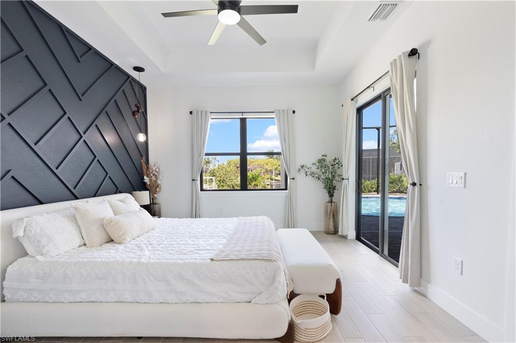 Bedroom featuring a tray ceiling, access to outside, ceiling fan, and light wood-type flooring