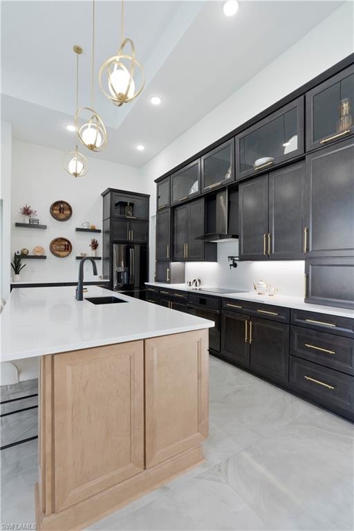 Kitchen with hanging light fixtures, dark cabinetry, a kitchen bar, stainless steel refrigerator with ice dispenser, and an island with sink