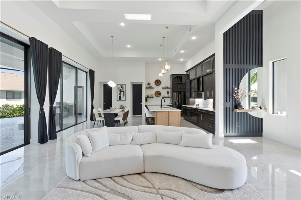 Living area with a high ceiling, a raised ceiling, light marble finish flooring, and recessed lighting