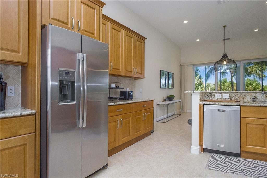 Kitchen with pendant lighting, light stone counters, and appliances with stainless steel finishes