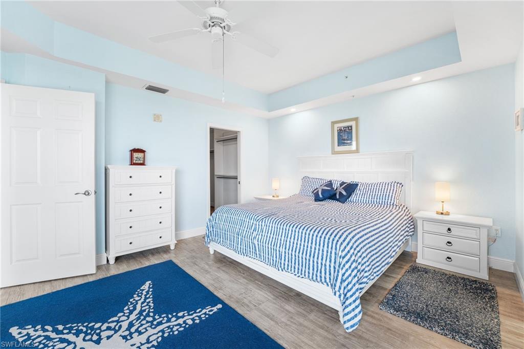 Bedroom featuring a tray ceiling, a walk in closet, wood finished floors, and recessed lighting