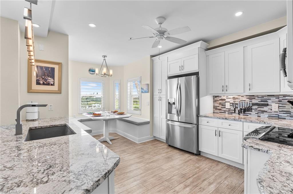 Kitchen featuring stainless steel fridge, light stone counters, white cabinets, recessed lighting, and decorative backsplash