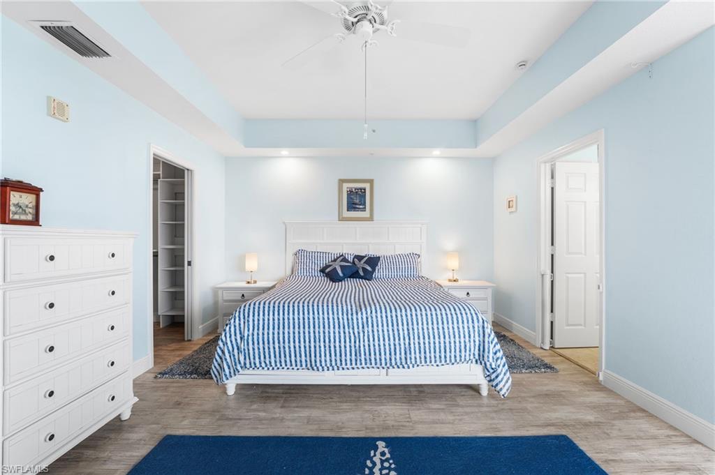 Bedroom with wood finished floors, a raised ceiling, a walk in closet, and a ceiling fan