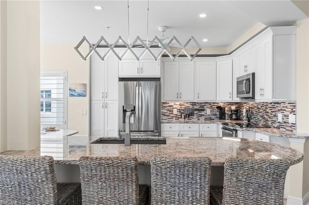 Kitchen with a breakfast bar area, stainless steel appliances, white cabinets, light stone counters, and backsplash