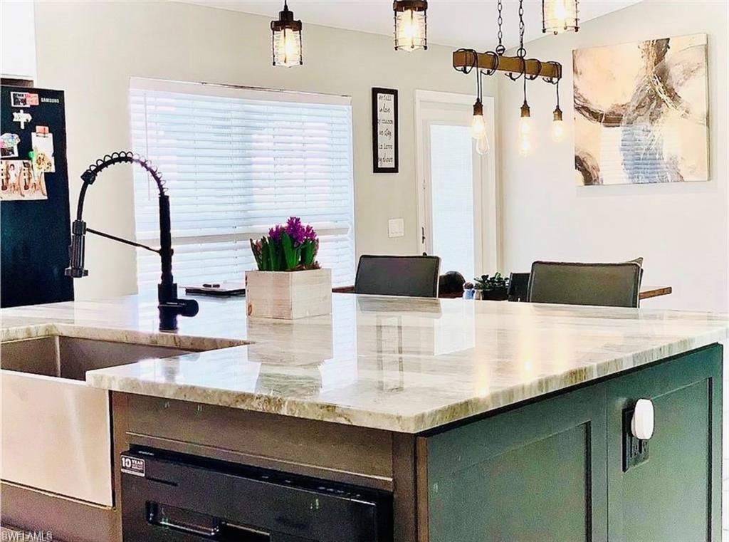 Kitchen with light stone counters, hanging light fixtures, green cabinets, and dishwashing machine