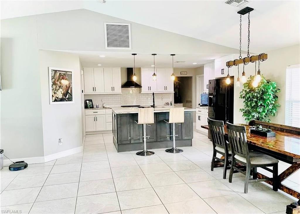 Kitchen featuring a center island with sink, white cabinets, a kitchen bar, tasteful backsplash, and vaulted ceiling