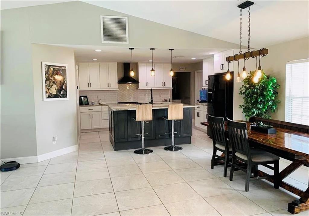 Kitchen with a center island with sink, decorative backsplash, pendant lighting, white cabinetry, and black fridge with ice dispenser