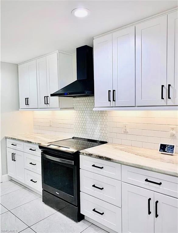 Kitchen featuring black range with electric cooktop, white cabinetry, decorative backsplash, and wall chimney exhaust hood