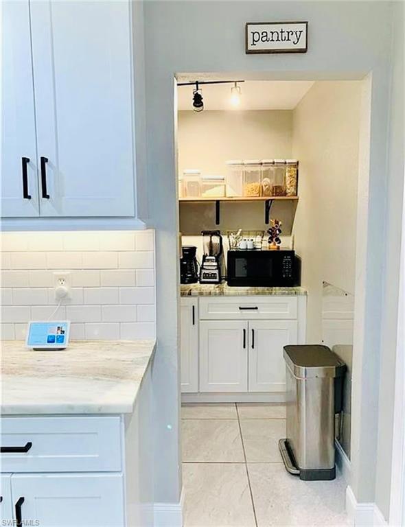 Bar featuring white cabinetry, light stone countertops, black microwave, light tile patterned floors, and backsplash