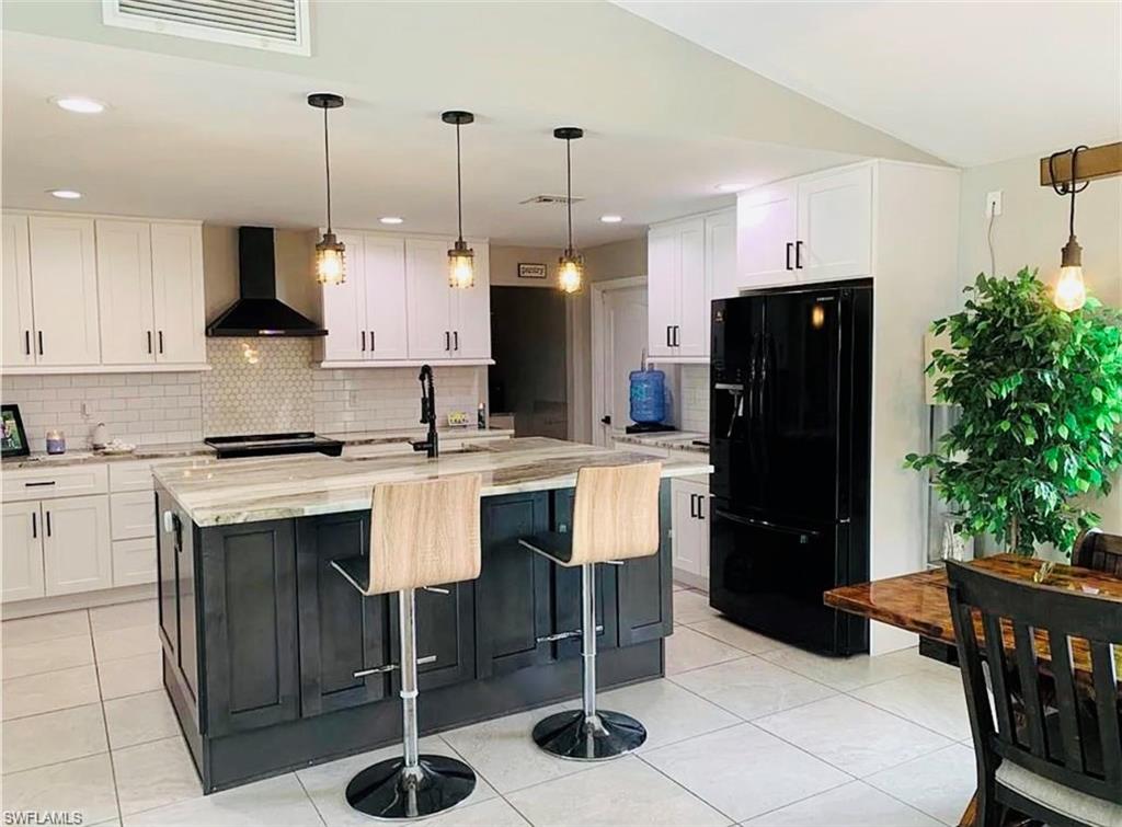 Kitchen with decorative light fixtures, black appliances, backsplash, light tile patterned floors, and wall chimney exhaust hood