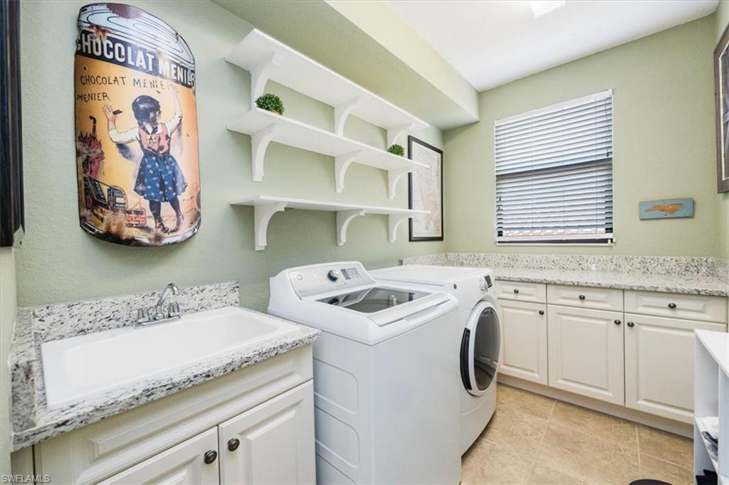 Laundry area featuring sink, light tile patterned floors, separate washer and dryer, and cabinets