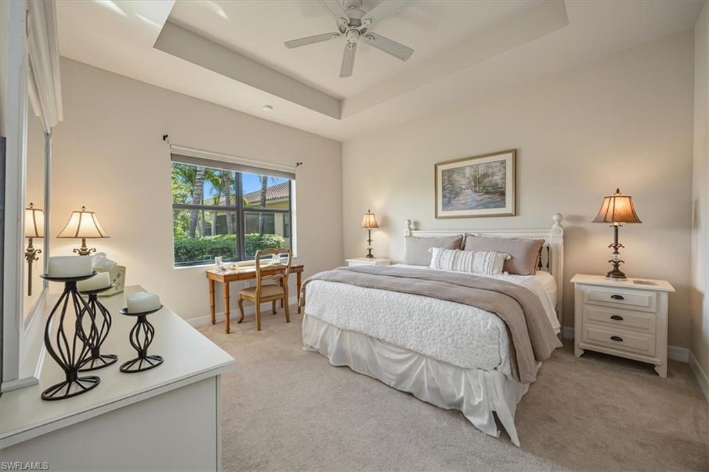 Bedroom with light colored carpet, a raised ceiling, and a ceiling fan
