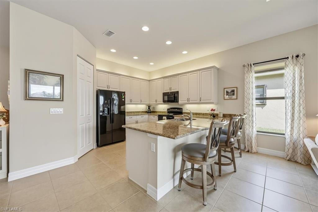 Kitchen featuring black appliances, light stone counters, a kitchen bar, light tile patterned floors, and recessed lighting