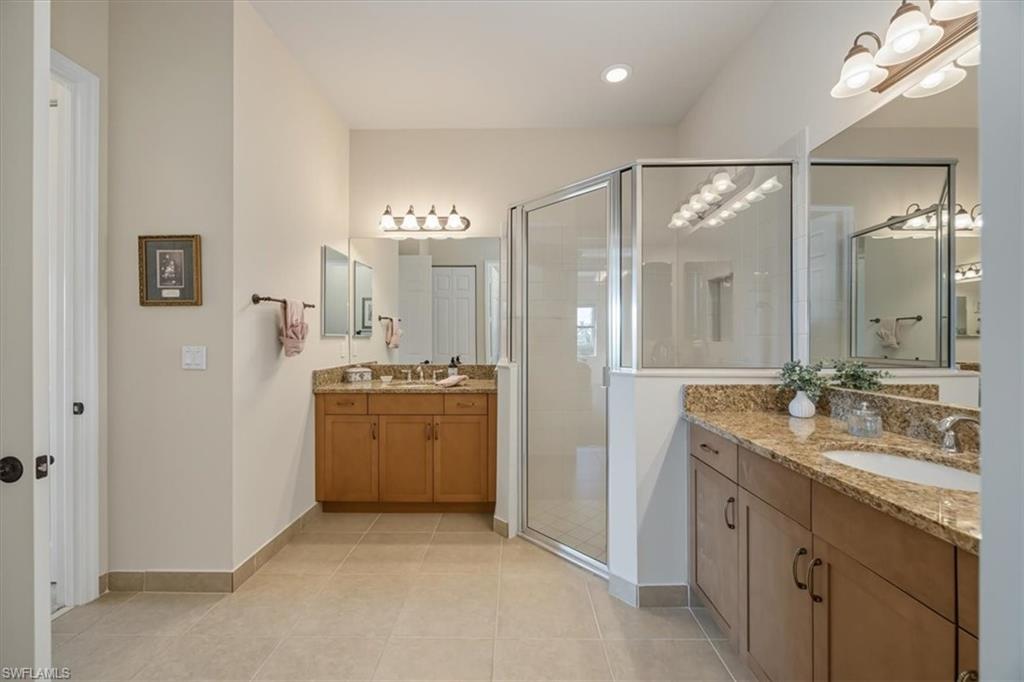 Full bathroom featuring a stall shower, light tile patterned flooring, and two vanities