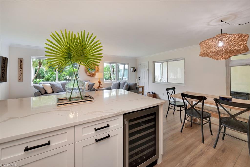 Bar with ornamental molding, light stone counters, white cabinets, beverage cooler, and light wood-style flooring