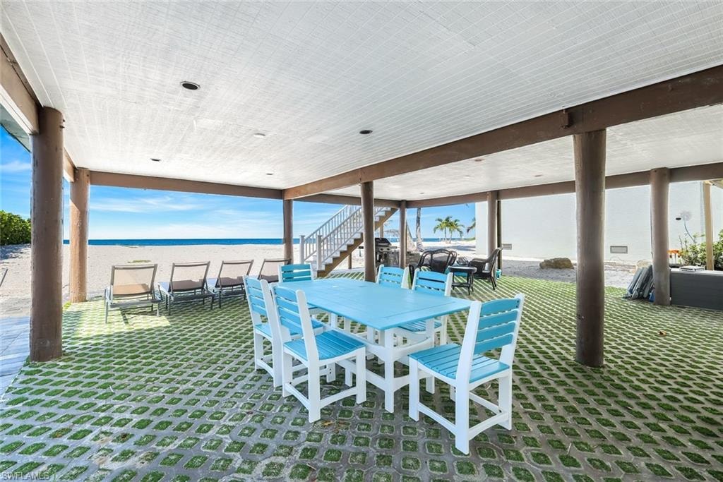 View of patio featuring view of water and beach, outdoor dining space, and stairs