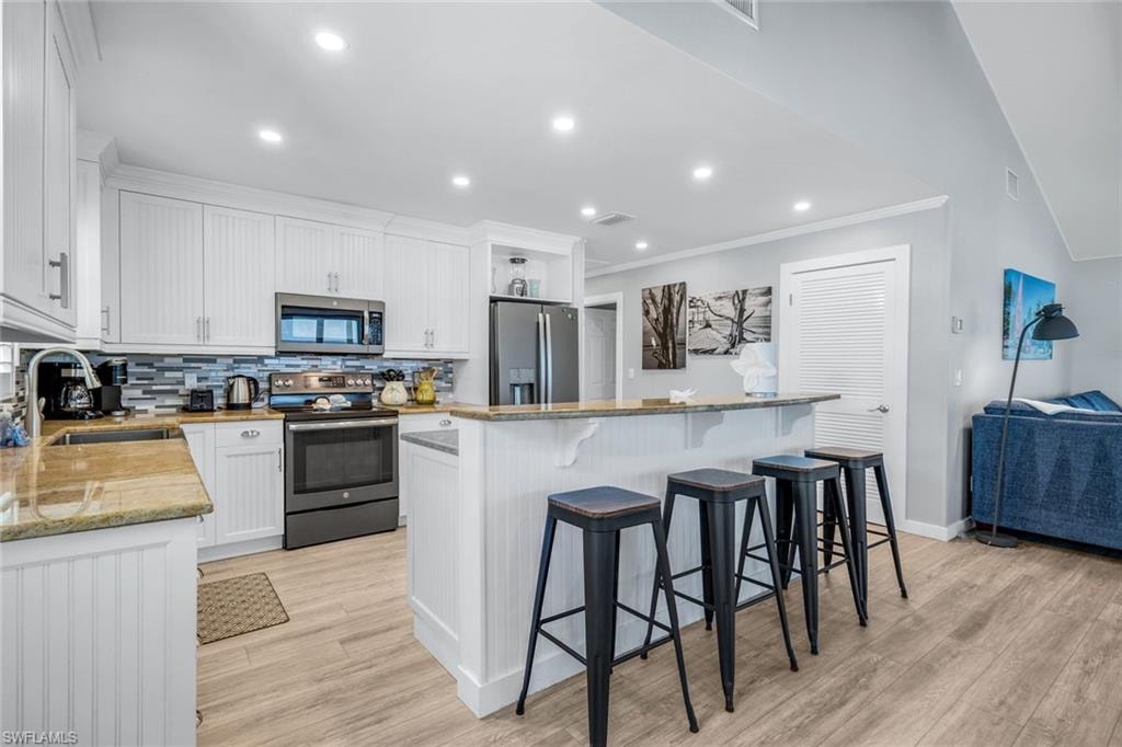 Kitchen with white cabinets, appliances with stainless steel finishes, decorative backsplash, light stone counters, and recessed lighting