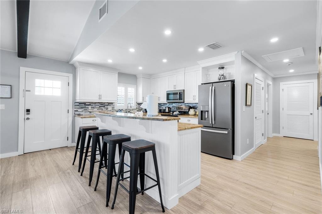 Kitchen featuring white cabinetry, stainless steel appliances, a breakfast bar, tasteful backsplash, and light wood-style floors