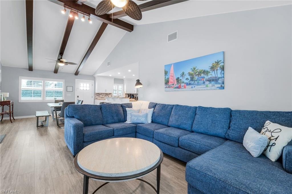 Living room with high vaulted ceiling, wood finished floors, beamed ceiling, and a ceiling fan
