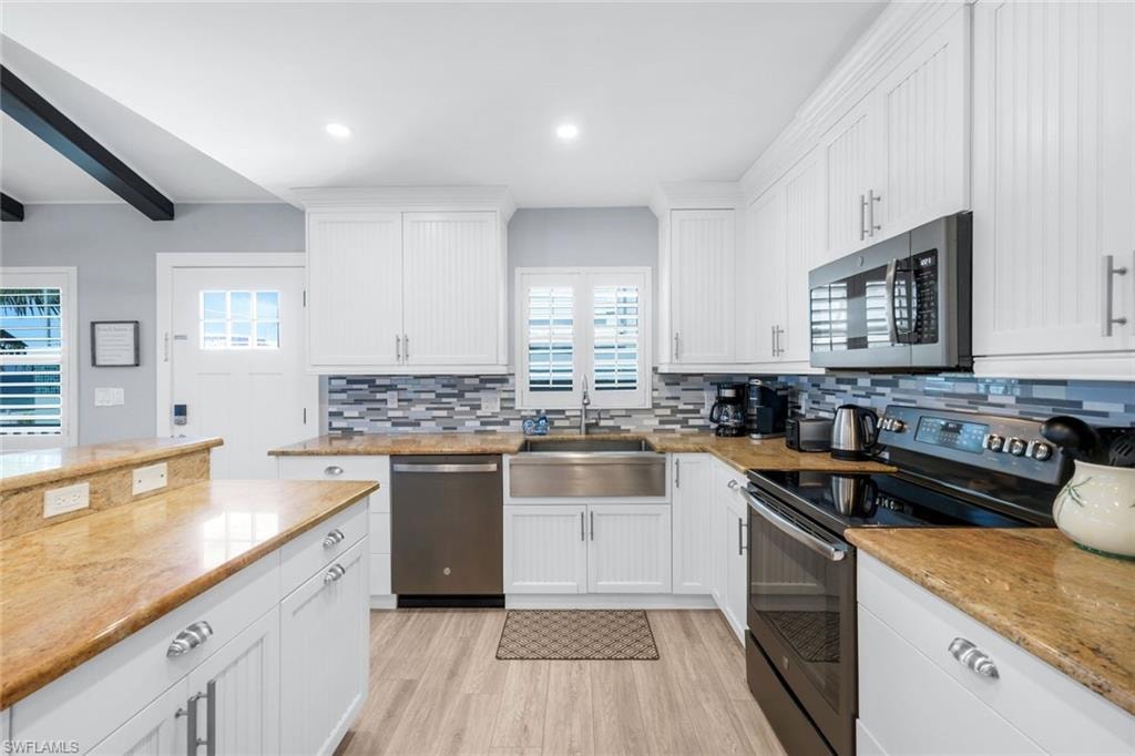 Kitchen featuring appliances with stainless steel finishes, white cabinetry, light wood finished floors, backsplash, and light stone countertops