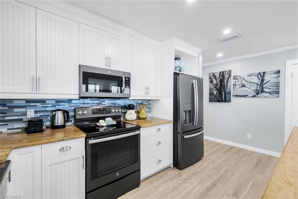Kitchen featuring appliances with stainless steel finishes, white cabinetry, crown molding, tasteful backsplash, and light wood-style floors