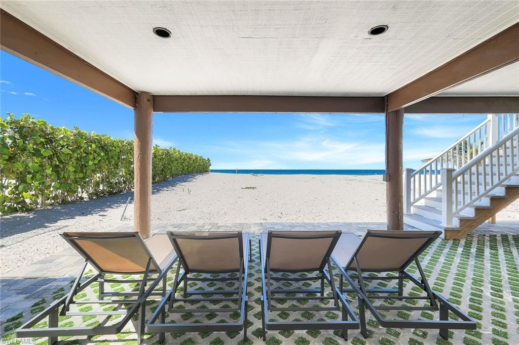 View of patio featuring view of water and beach and stairs