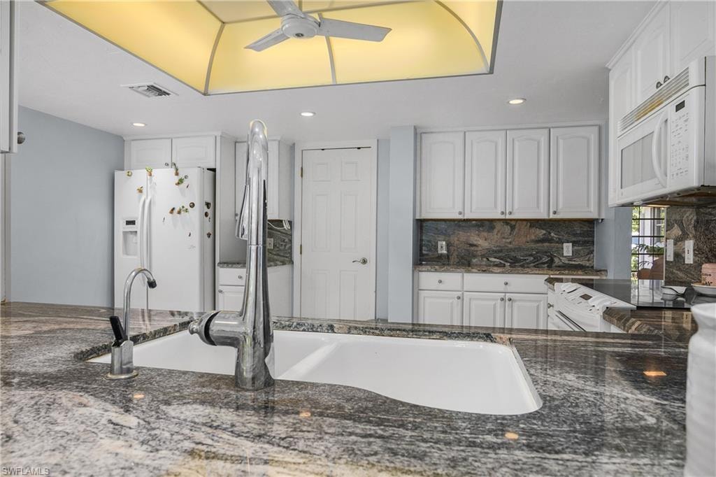 Kitchen featuring dark stone countertops, white appliances, white cabinets, decorative backsplash, and a ceiling fan