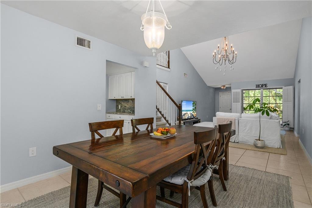 Dining area with light tile patterned floors, stairway, high vaulted ceiling, and a chandelier