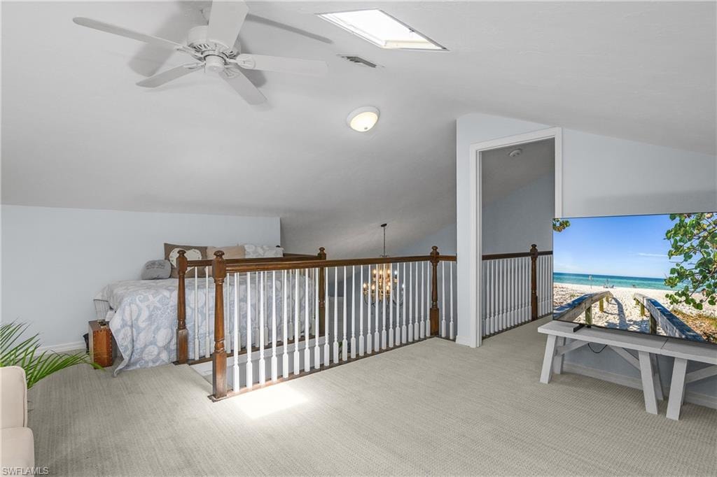 Bonus room with lofted ceiling, light carpet, view of water and beach, a chandelier, and ceiling fan