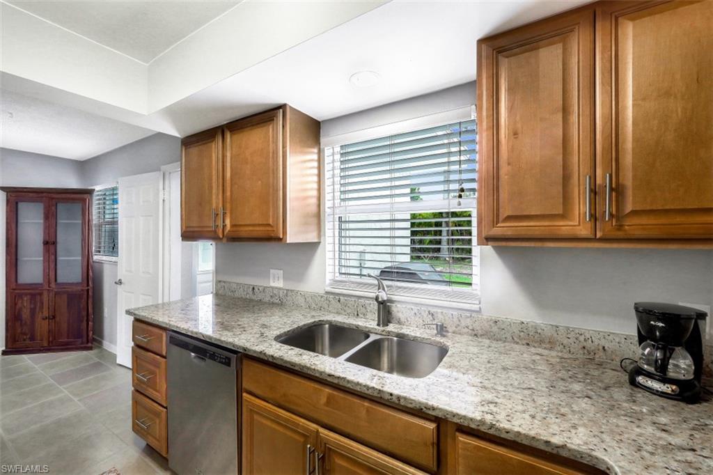 Kitchen featuring brown cabinets, light stone counters, stainless steel dishwasher, and light tile patterned flooring