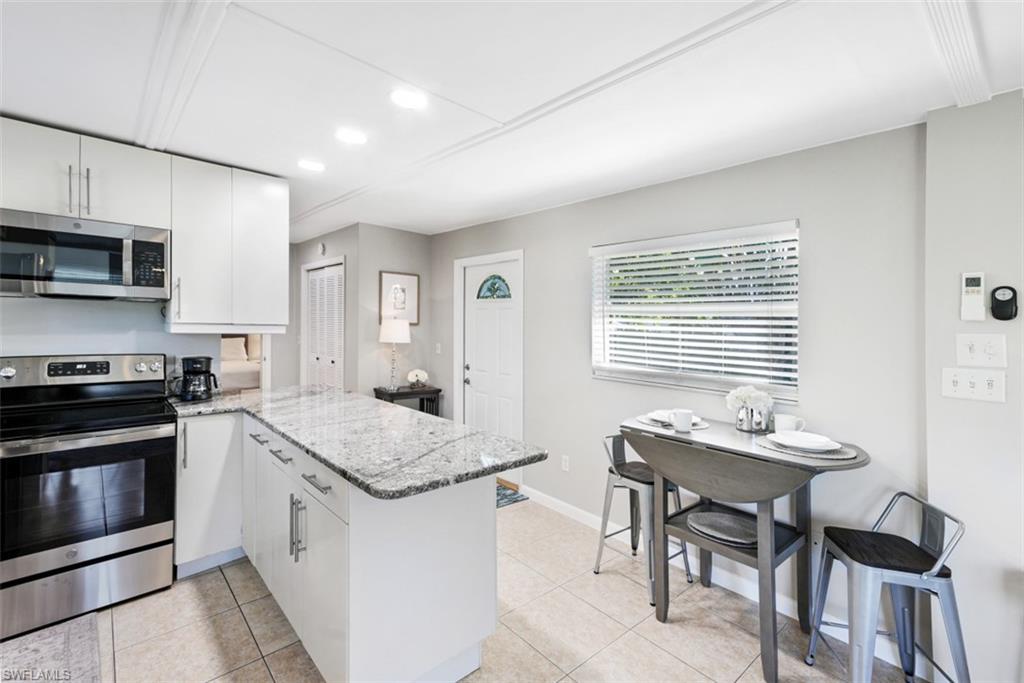 Kitchen with stainless steel appliances, a peninsula, light stone counters, white cabinetry, and recessed lighting