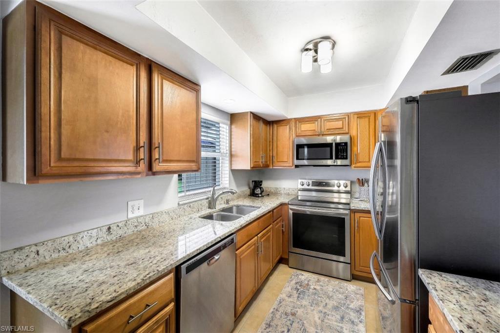 Kitchen featuring brown cabinetry, appliances with stainless steel finishes, light stone counters, and light tile patterned floors