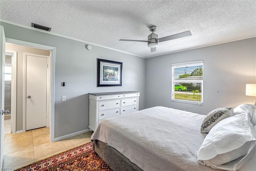 Bedroom featuring a textured ceiling, ornamental molding, ceiling fan, and light tile patterned flooring