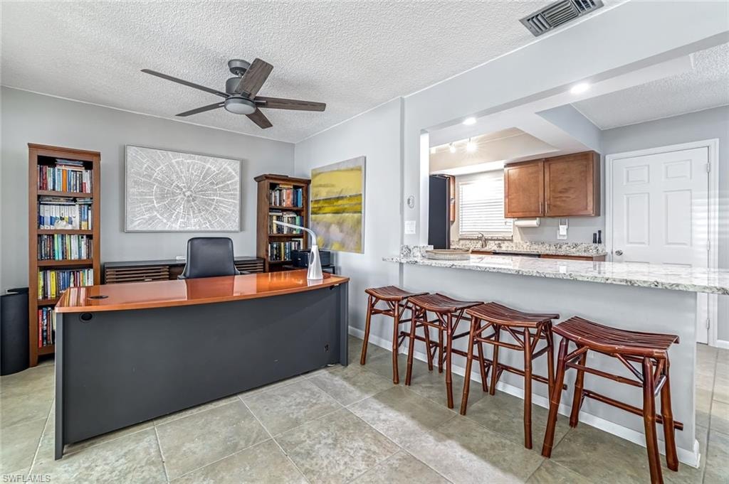 Office space with a textured ceiling, ceiling fan, and light tile patterned flooring