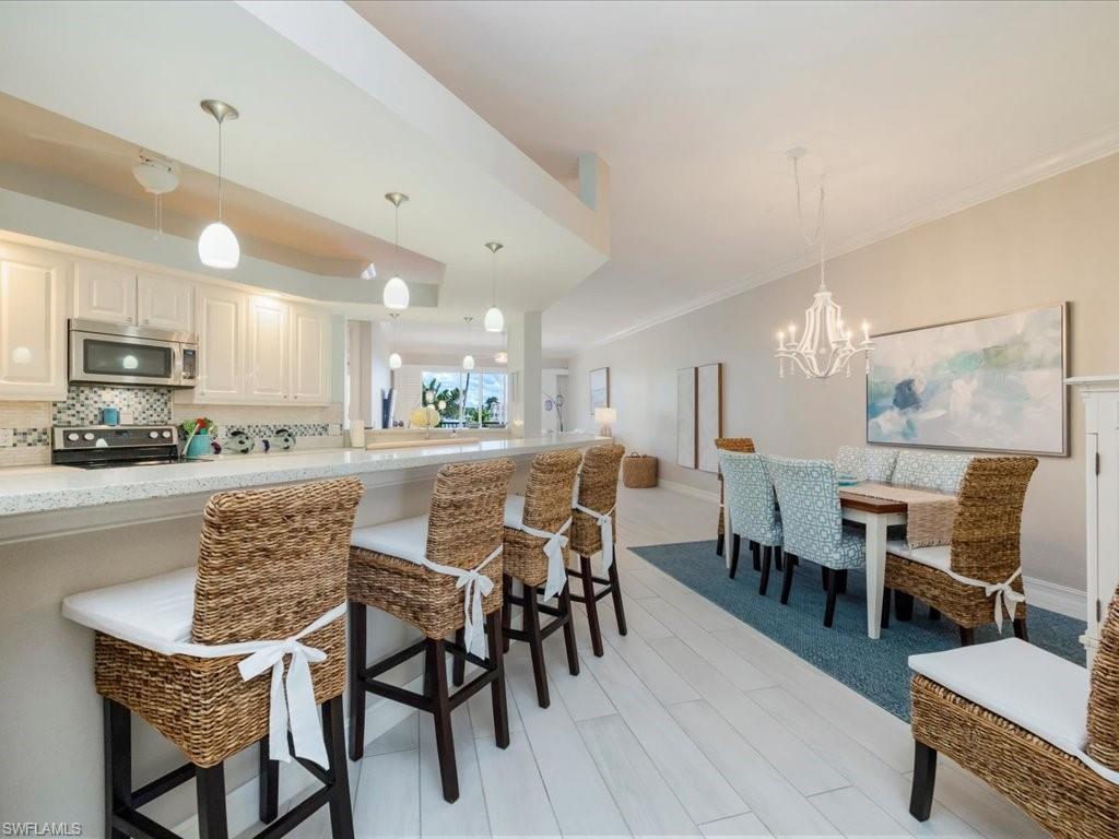 Kitchen featuring tasteful backsplash, appliances with stainless steel finishes, hanging light fixtures, a kitchen breakfast bar, and a chandelier