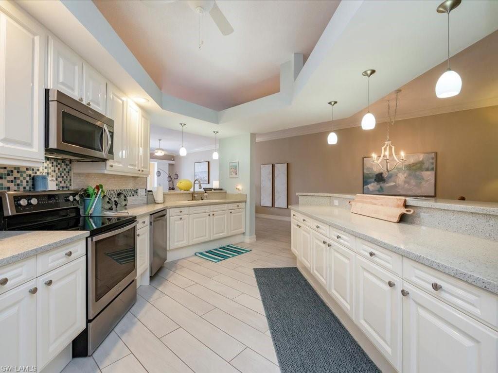 Kitchen featuring appliances with stainless steel finishes, a tray ceiling, light stone counters, white cabinets, and crown molding