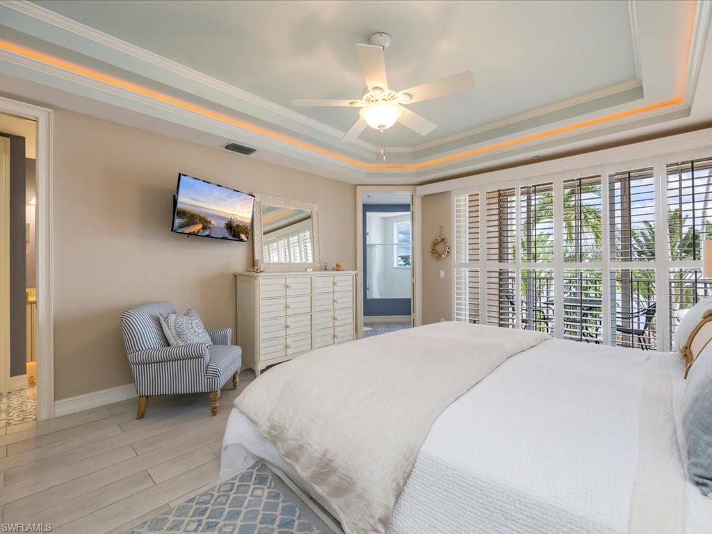 Bedroom with a raised ceiling, multiple windows, crown molding, wood finished floors, and a ceiling fan