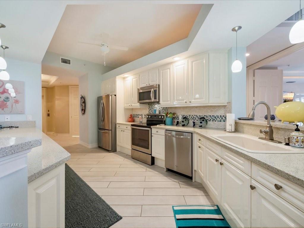Kitchen with decorative light fixtures, light stone counters, stainless steel appliances, and decorative backsplash