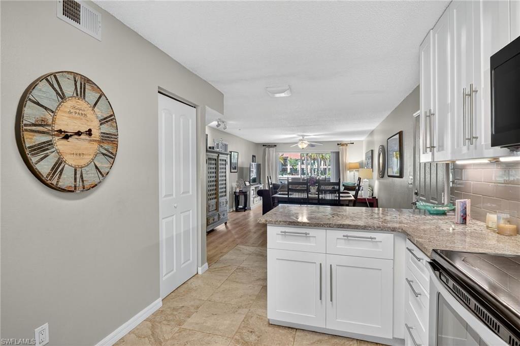 Kitchen featuring a peninsula, open floor plan, light stone counters, white cabinetry, and stainless steel range with electric cooktop